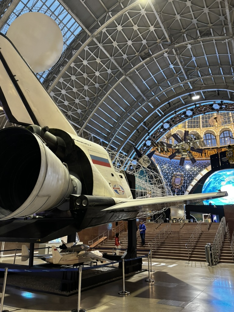 A spacecraft exhibit beneath a vaulted exhibition hall roof