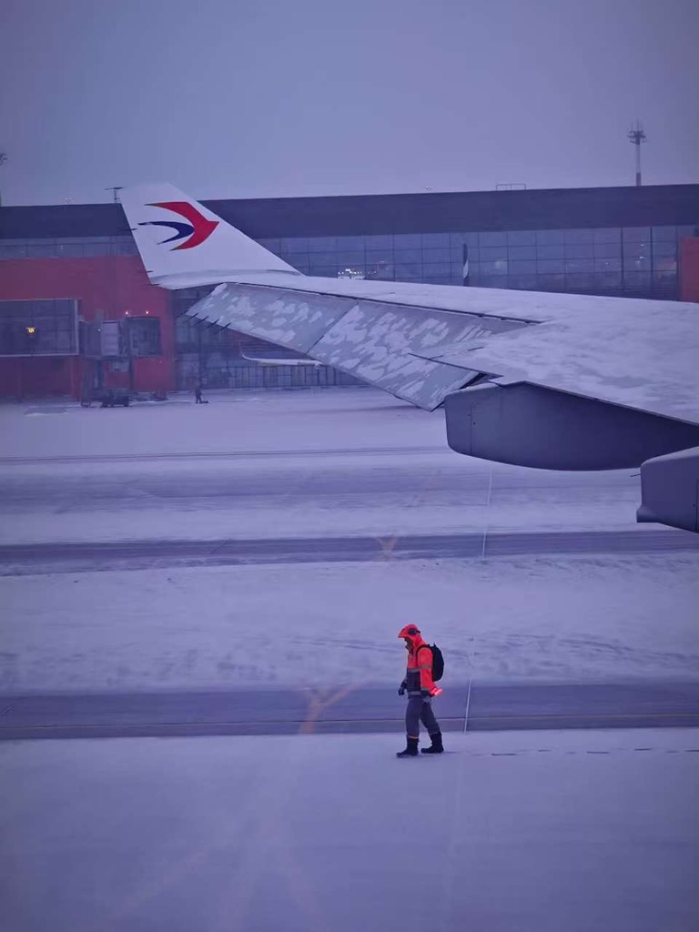 An aircraft wing and airport worker on a snowy apron