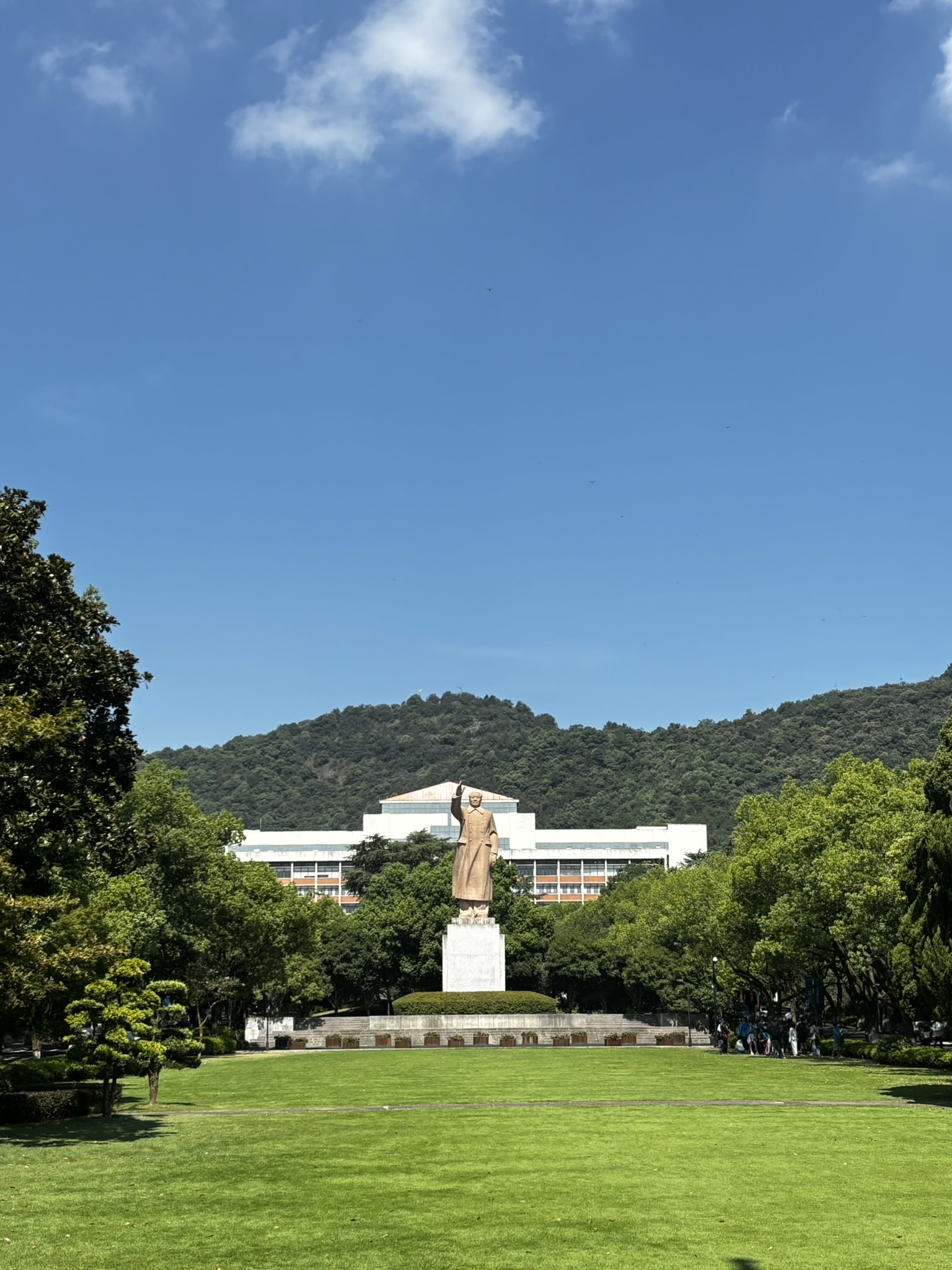 A campus lawn and statue with wooded hills behind